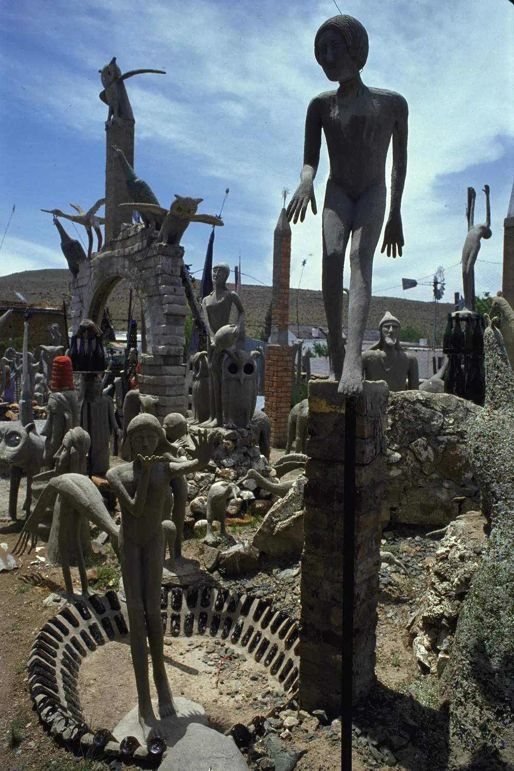 Cement and glass figures in the Camel Yard at The Owl House in Nieu-Bethesda, including standing human forms and a stone archway