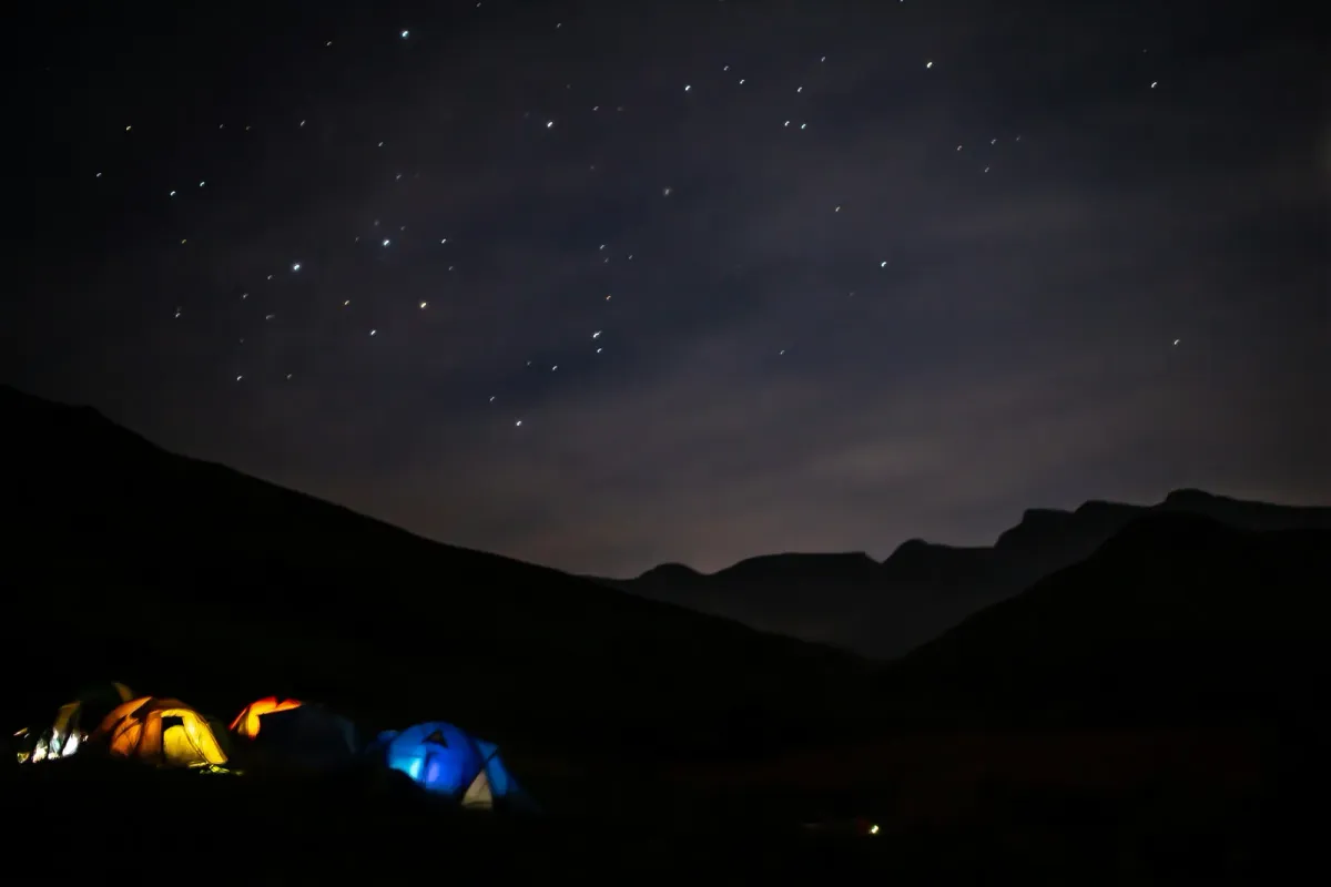 Tents glowing under a starry night sky below the Drakensberg mountains at Giants Castle, South Africa