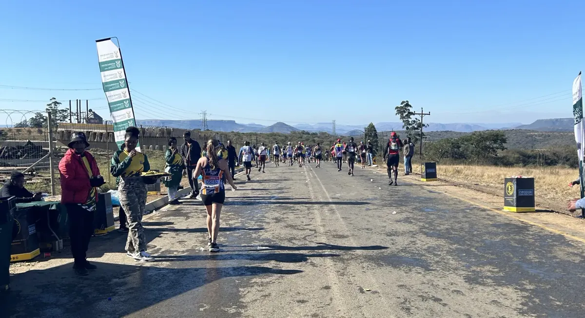 Runners spread out along an open tar road through the KwaZulu-Natal hills during the Comrades Marathon, with supporters watching from the roadside.