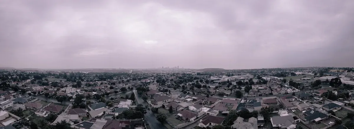 Aerial view over Johannesburg suburbs with the city skyline hazy in the distance under an overcast sky