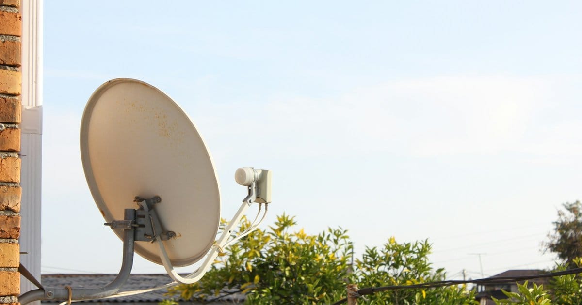 Two satellite dishes mounted on a residential wall against a clear sky