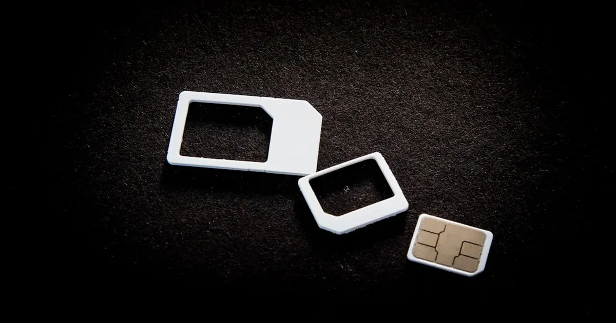 A nano SIM card lying next to two SIM card adaptors on a dark textured surface