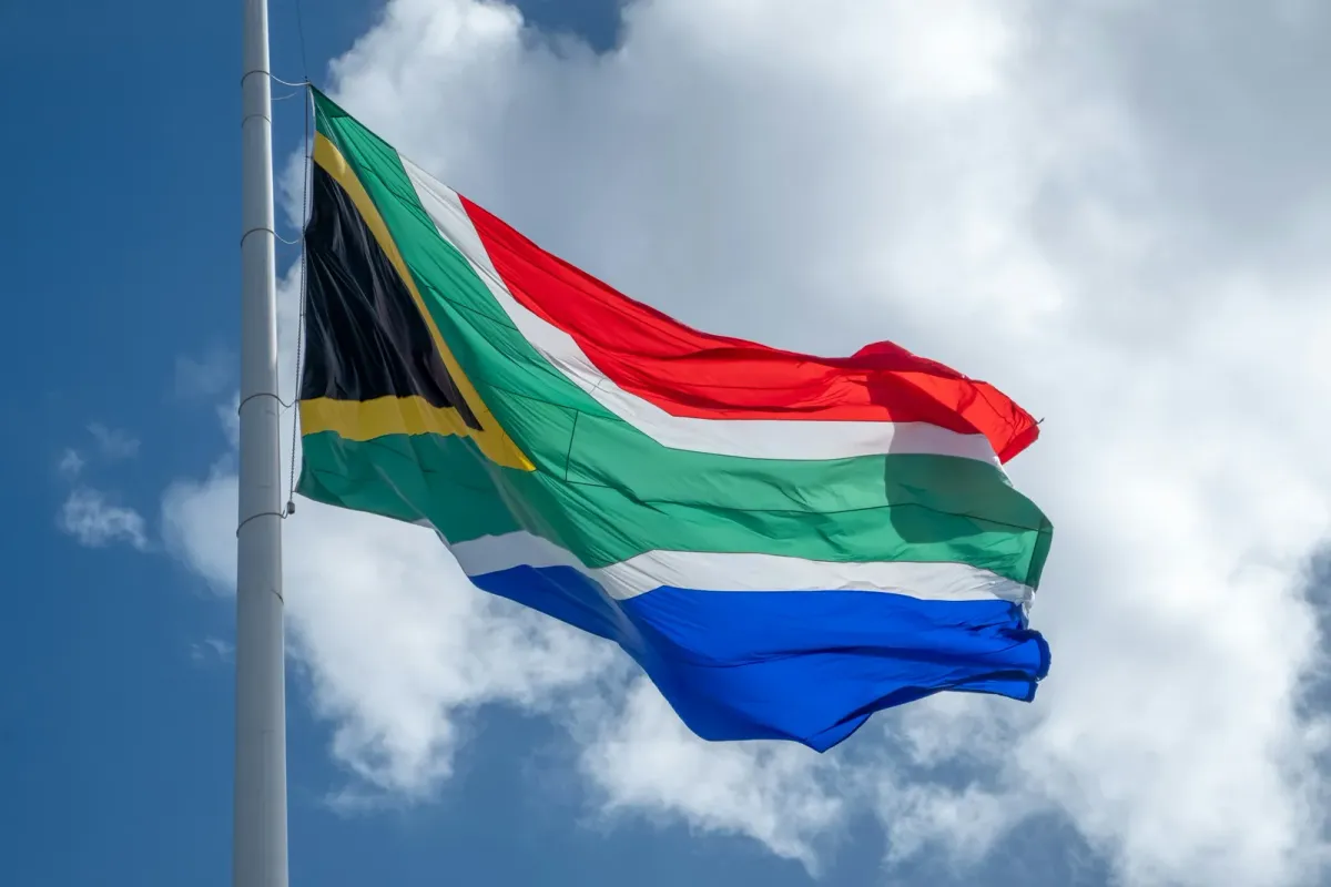 The South African flag flying against a blue sky with white clouds.